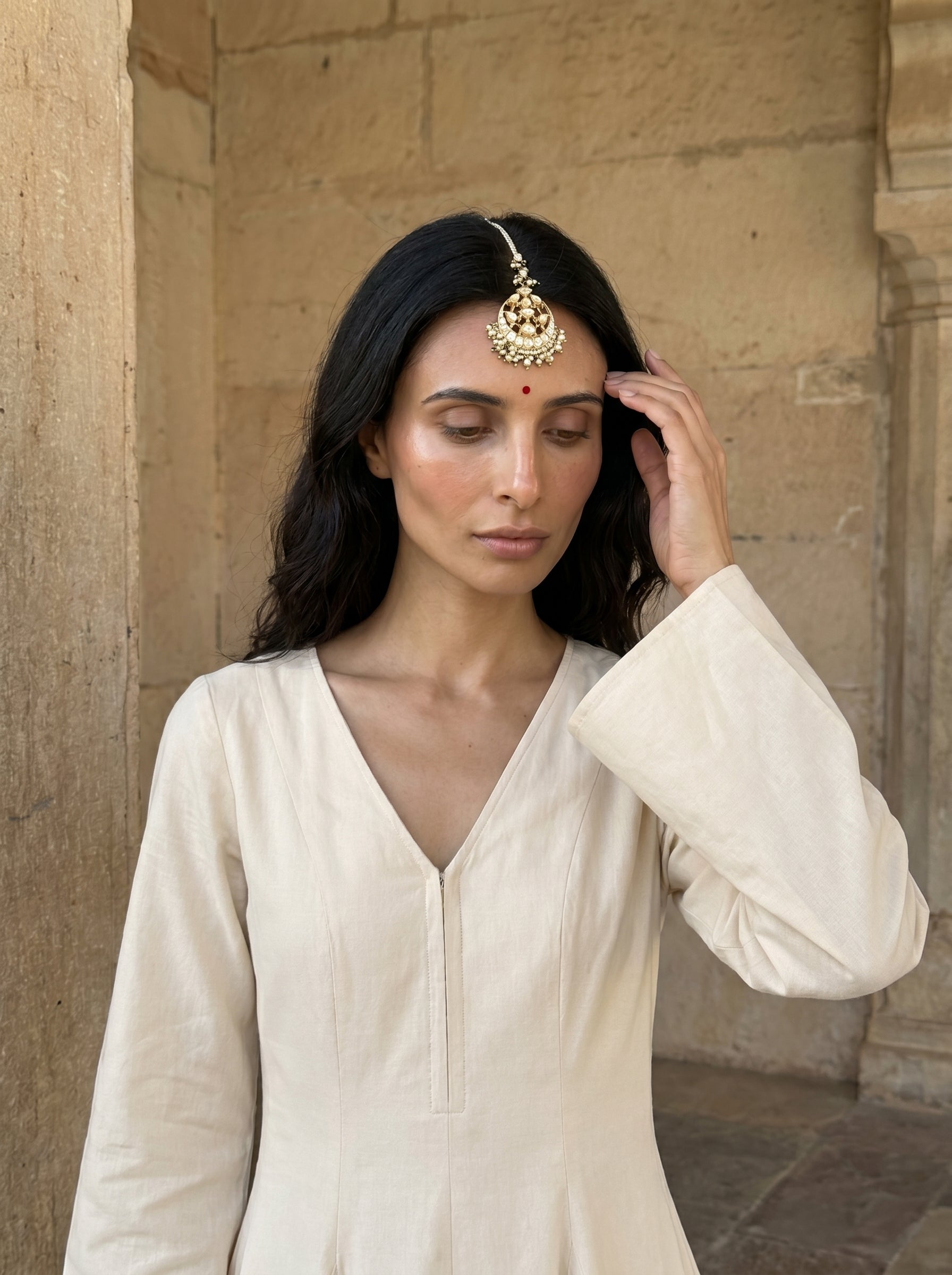 Woman wearing a traditional gold headpiece against a stone wall.